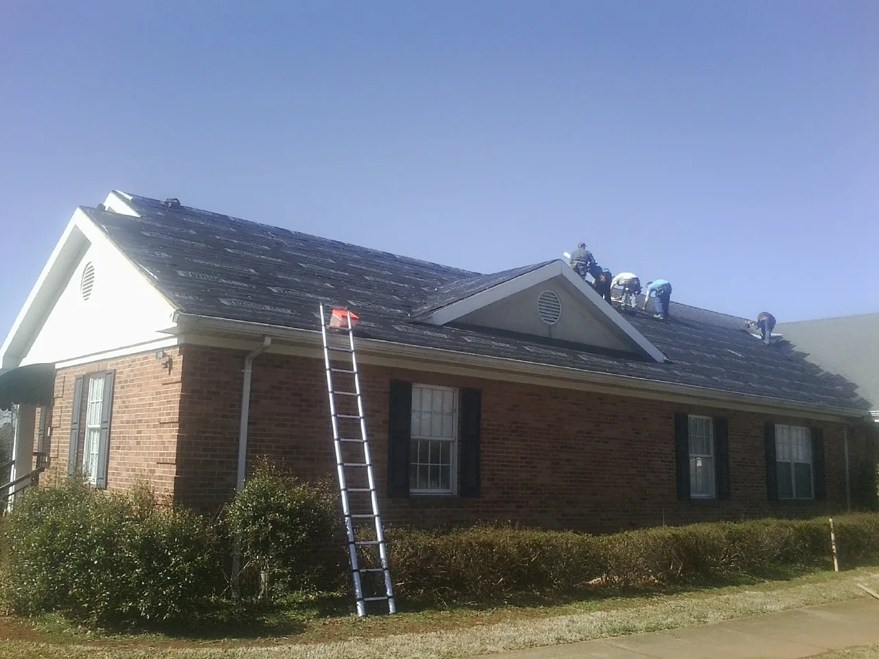 Crew tearing shingles off a brick ranch roof with a ladder set — Emergency Roof Repair work by our crew in Inverness