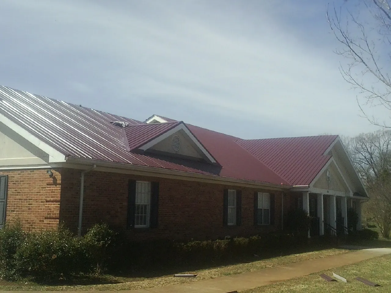 Red metal roof with gabled entries on a long brick building, from a Hail Damage Roof Repair job in Inverness