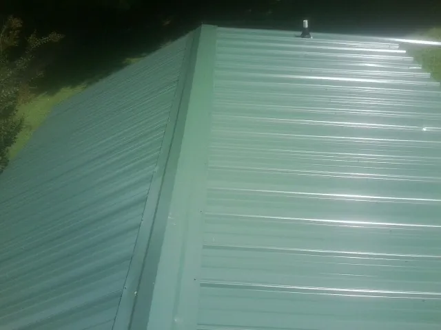 New green metal panels meeting at the ridge of a roof — Flat Roof Repair work by our crew in Inverness