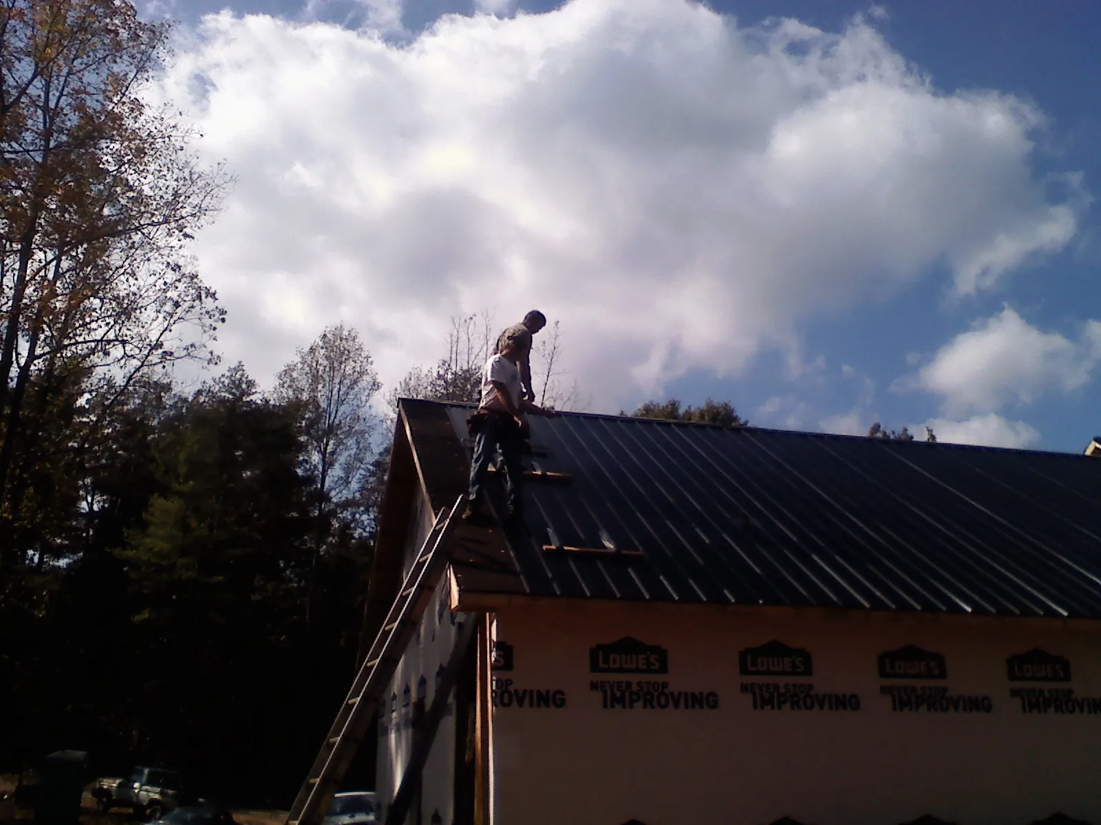 Roofer fastening dark metal panels high against a cloudy sky, from a Roof Inspection job in Inverness