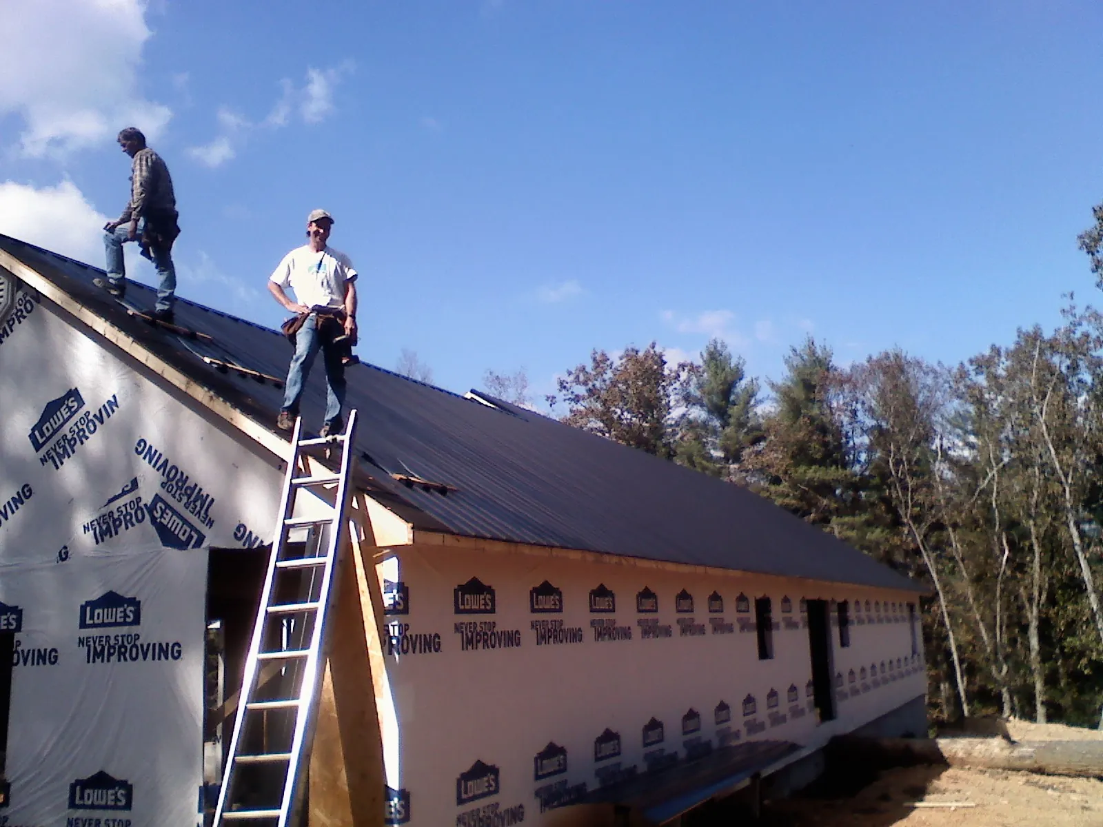Two roofers standing on a long dark metal roof over a wrapped building in Inverness