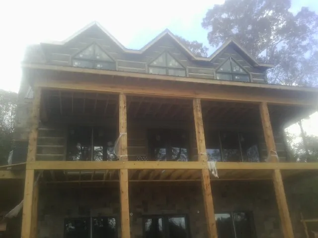 Dormers and porch framing on a large log home under construction — Roof Coating work by our crew in Inverness