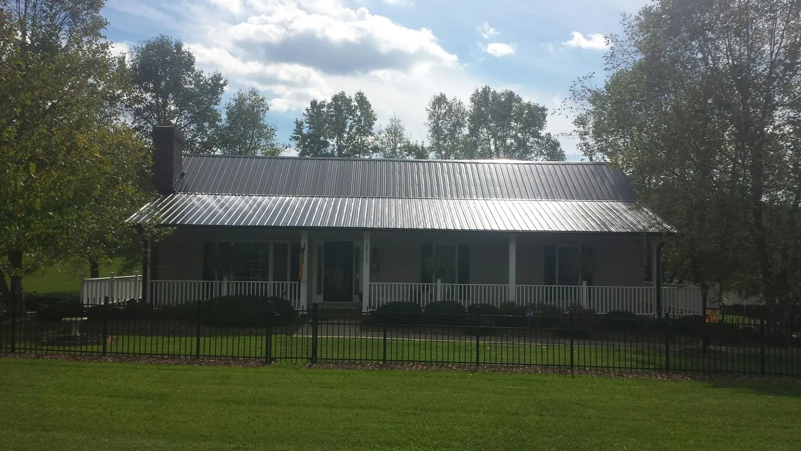 Gray metal roof on a brick ranch with a full width front porch — Gutter Guard Installation work by our crew in Inverness