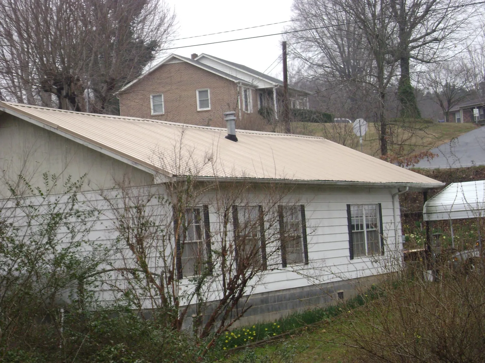 Tan metal roof on a white sided house set into a hillside — Commercial Roofing by Roofing Brothers in Inverness
