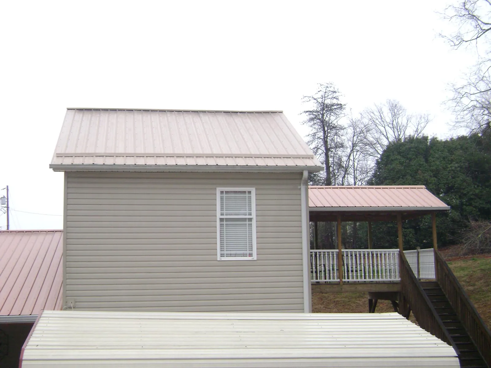 Tan metal roofs on a two story addition and attached porch, from a Roof Replacement job in Inverness